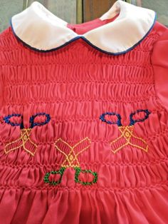 a red dress with blue and yellow embroidered letters on it, sitting on a chair