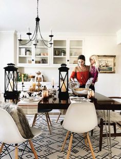 two women sitting at a dining room table with white chairs and an area rug on the floor