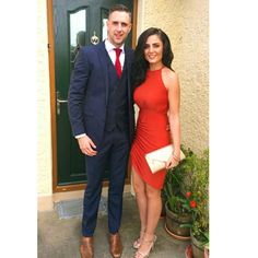 a man in a suit and woman in a red dress posing for a photo outside