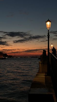 a person standing on a pier next to the ocean at night with a street light in front of them