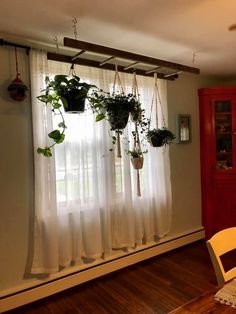 some plants are hanging on the window sill in front of a table and chair