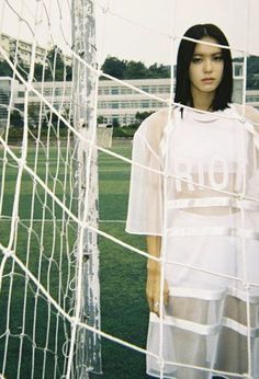 a woman standing in front of a soccer goal wearing a white shirt with the word riot written on it