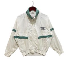 a white jacket with green trims hanging from a hanger on a clothes rack