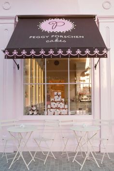 two white folding chairs sitting in front of a pink building with a black awning