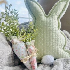 a stuffed bunny sitting on top of a blanket next to pillows and flowers in vases