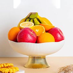 a white bowl filled with lots of fruit next to some crackers on a table