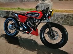 a red and black motorcycle parked on the side of a road next to a stone wall