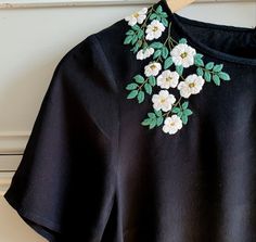 a black t - shirt with white flowers on it hanging from a wooden hanger