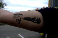 a man with a tattoo on his arm holding a coffee cup and saucer in one hand