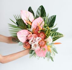 a woman holding a bouquet of flowers in her hands with greenery on the side