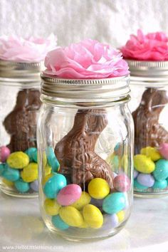 three mason jars filled with chocolate bunny candies and pink flowers on top of them