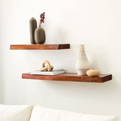 two wooden shelves with vases and books on them next to a white couch in a living room