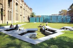 people sitting on benches in the middle of a grassy area next to a large building