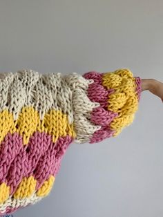 a person holding up a knitted blanket in the air with their hand on it