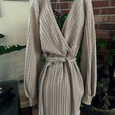 Wrap Yourself Up In This Cute And Casual Cable Knit Sweater Dress Perfect For Pumpkin Patches Or Festivals! It Features Long Sleeves With Banded Cuffs, A Plunge Surplice V-Neckline And V-Cut Back, A Tie-Waist Belt, And A Short Form-Hugging Fit. Complete The Look In Trendy Knee-High Boots. Cozy Long Fitted Dress, Knit Dress For Loungewear, Chic Cable Knit Sweater Dress For Spring, Cozy Fitted Knitted Dresses, Cozy Knitted Fitted Dress, Cable Knit Long Sleeve Dress, Cozy Knitted Spring Dresses, Cozy Beige Knit Dress, Beige Cable Knit Dress