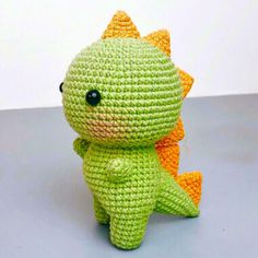 a crocheted green and orange stuffed animal sitting on top of a gray surface