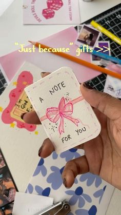 a hand holding a note with a pink bow on it and some other items in the background