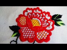 a close up of a red flower on a white cloth with green and yellow accents