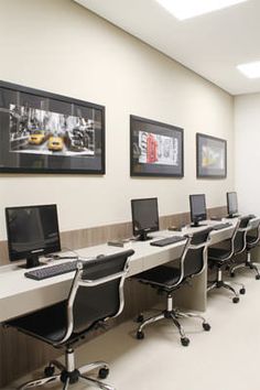 an office with several computers on the desks in front of them and two framed pictures above it