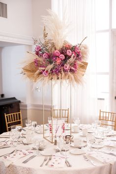 there is a tall centerpiece with flowers and feathers on it at the head table