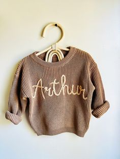 a brown sweater with the word arthrur written on it hanging from a hanger