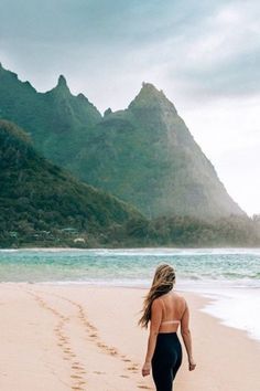 a woman is walking on the beach with mountains in the background and footprints in the sand