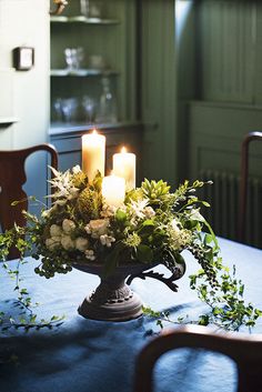 candles are lit on a table with flowers and greenery in the center, surrounded by chairs