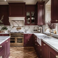 a kitchen with red cabinets and marble counter tops, an oven in the center is surrounded by wood flooring