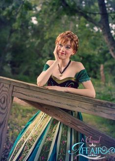 a woman in a dress leaning on a wooden fence with her hand near her face