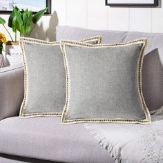 two gray pillows sitting on top of a couch next to a vase with yellow flowers