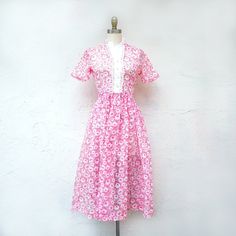 1950's dress in pink and white floral organdy. It has a full tea length skirt gathered to a natural waist. With short sleeves it has pearl buttons to the waist and a side metal zipper. The fabric is translucent. So sweetly feminine, it would be a lovely bridesmaid dress for a vintage wedding, or recital, reception or dance dress. There are no darts. It is a teen or very petite dress. So sweetly feminine. Fits like a current XX Small 0 to 00 Measurements with room for comfort: Bust up to: 32 inch 1950s Vintage Short Sleeve Dress For Spring, 1950s Vintage Spring Dress With Short Sleeves, 1950s Short Sleeve Vintage Dress For Garden Party, 1950s Pink Vintage Dress With Short Sleeves, White Vintage 1950s Style Dress With Short Sleeves, 1950s Style Short Sleeve Vintage Dress For Spring, 1950s Style White Vintage Dress With Short Sleeves, White Short Sleeve Vintage 1950s Style Dress, Pink Floral Print Vintage Dress With Short Sleeves