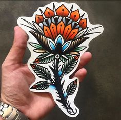 a hand holding a sticker with an orange and blue flower on it