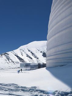 two people are walking in the snow near a large structure on top of a mountain