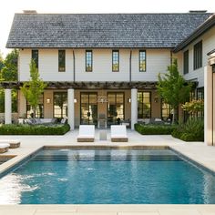 an outdoor swimming pool with lounge chairs and umbrellas in front of a large house