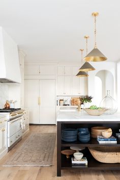 a kitchen with white cabinets and wooden floors, an island in the middle has blue dishes on it