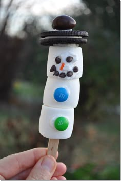 a hand holding a marshmallow snowman on a stick