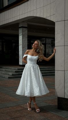 a woman in a white dress leaning against a wall