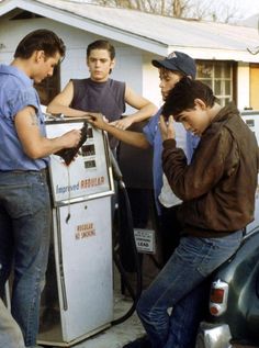 three boys are filling up their cars at a gas station in front of a house