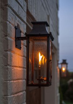 an old fashioned lantern hanging on the side of a building with two lit candles in it