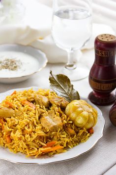 a white plate topped with rice and vegetables next to two wine glasses on a table