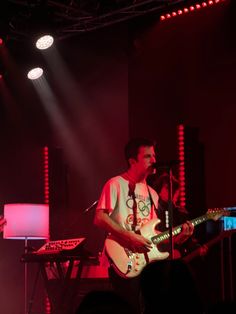 a man that is standing up with a guitar in his hand and lights on behind him