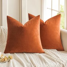 two orange pillows sitting on top of a white couch next to a cup of coffee