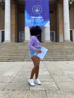 a woman standing in front of a building holding a folder and looking at the ground