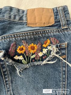 the back pocket of a pair of jeans with embroidered flowers on it and frayed edges