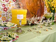 a table topped with lots of glasses filled with liquid and limes on top of plates