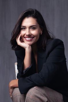 a woman sitting down with her hand on her chin and looking at the camera while smiling