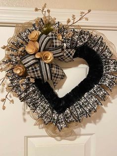 a heart shaped wreath with black and white ribbon hanging on the front door, decorated with gold buttons