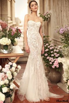 a woman standing in front of flowers wearing a wedding dress