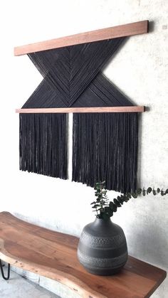 a wooden table topped with a black vase filled with flowers and fringed wall hangings