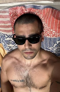 a shirtless man with no shirt and sunglasses on laying in bed next to a teddy bear